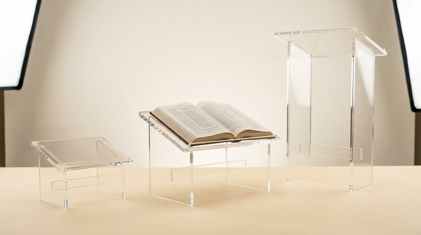 Three clear lucite shtenders of different sizes arranged by size on a neutral studio background