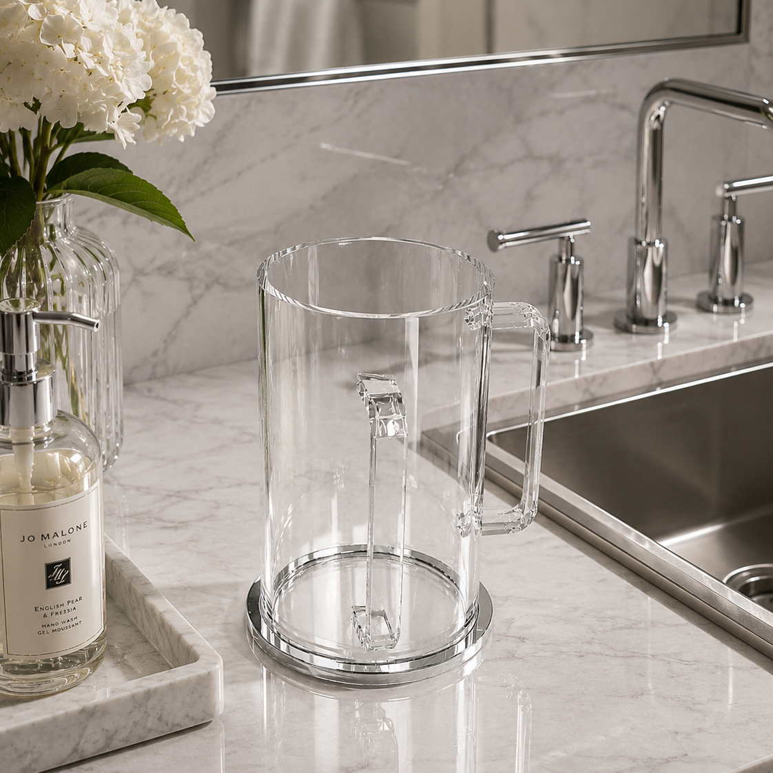 Clear lucite washing cup on a marble bathroom counter with flowers and soap dispenser -Zstander