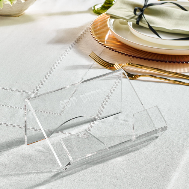 A clear lucite Haggadah holder displayed on a table set for Passover with seder plates and utensils - Zstander