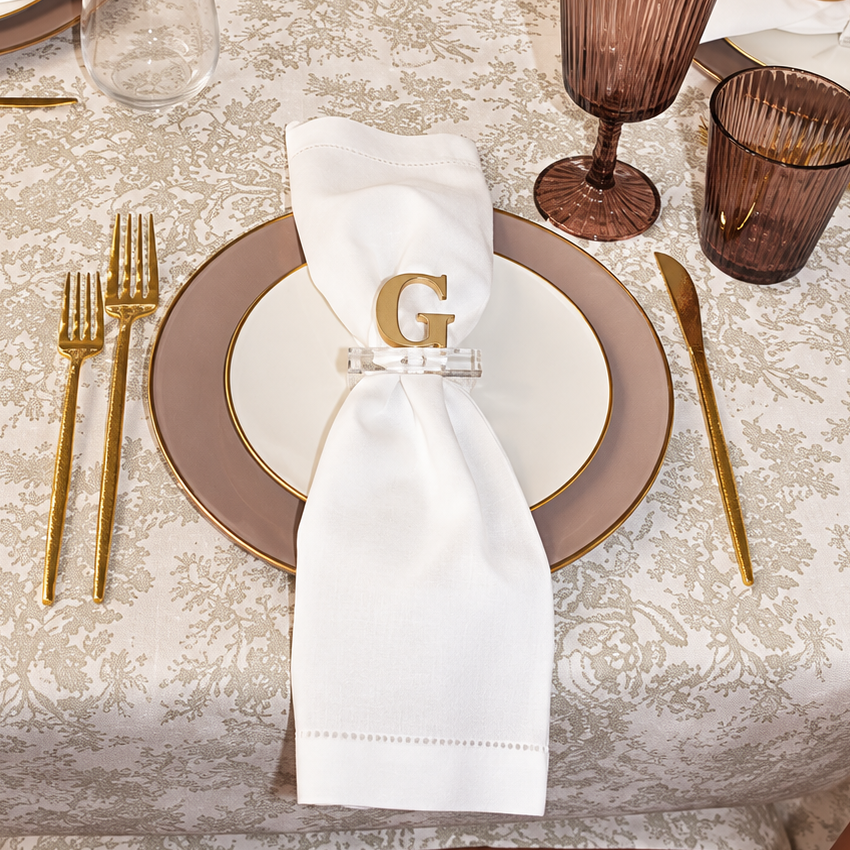 Gold G napkin ring on a pink plastic plate and floral tablecloth.