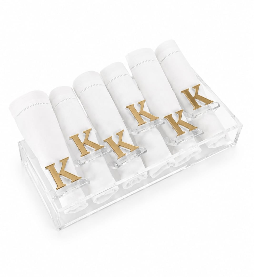 six white rolled napkins in a clear acrylic holder, each with a gold letter K on top, photographed on a white background - Zstander