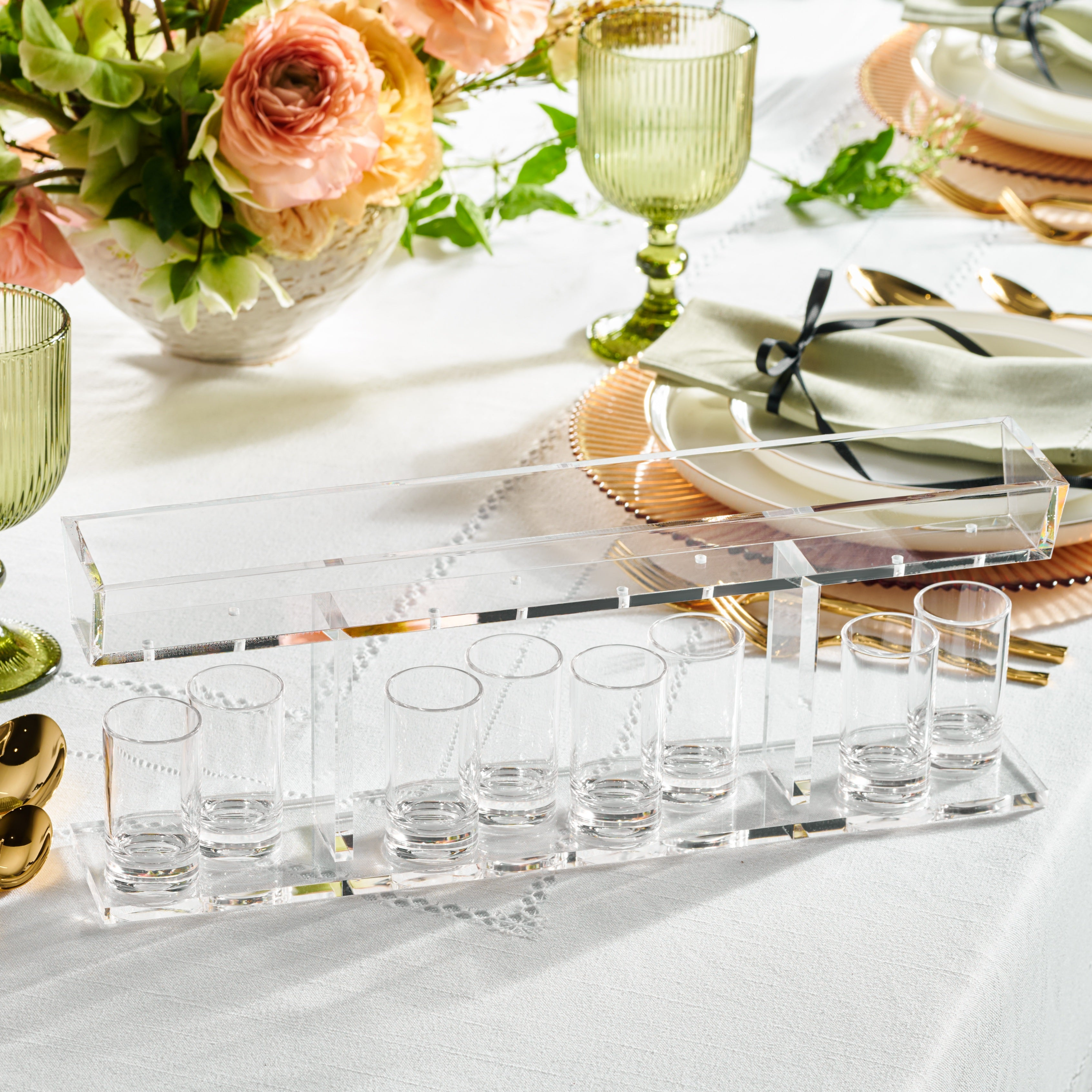 Row of shot glasses on a clear tray, set against a blurred background with flowers and decor - Zstander