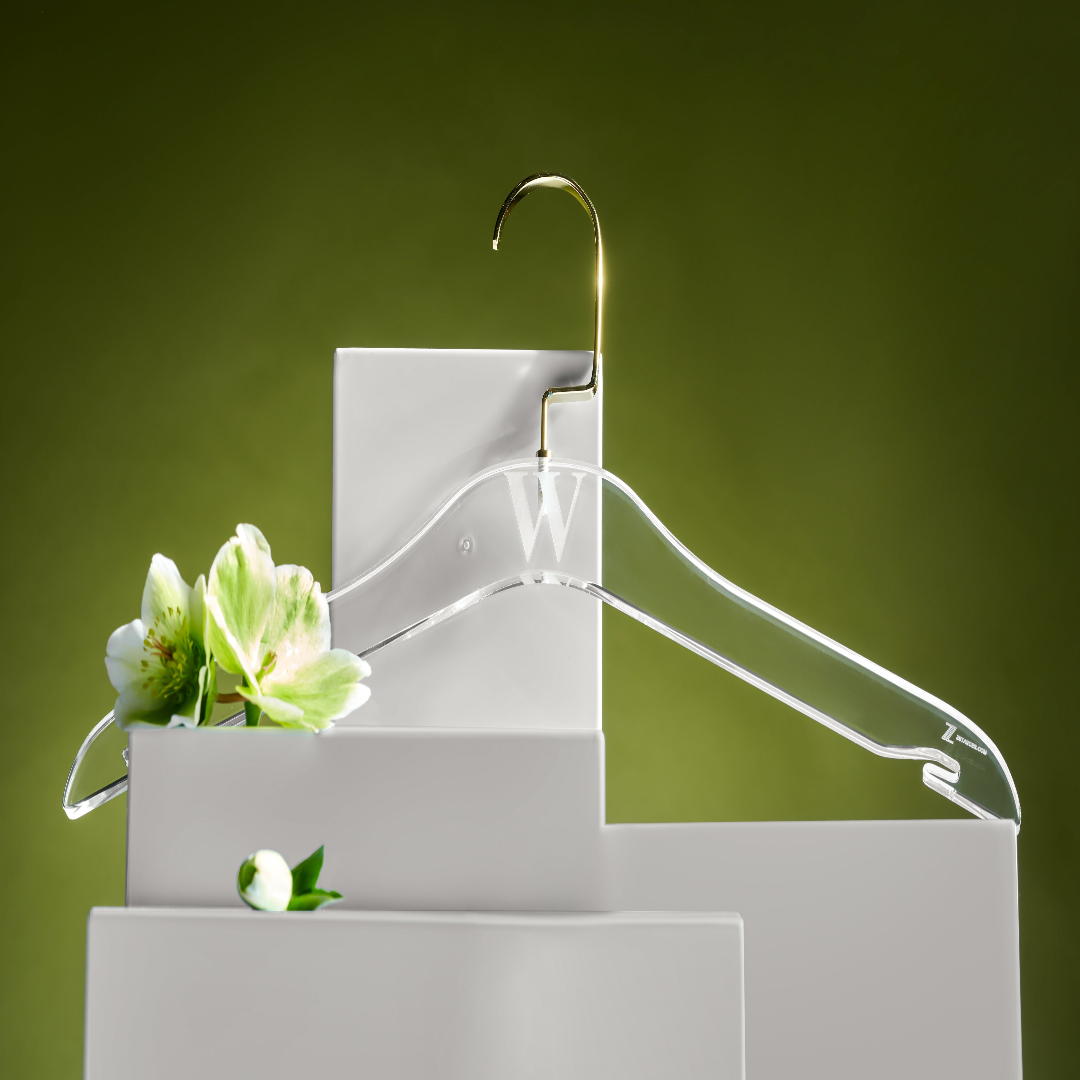 Clear lucite hanger on a white pedestal with green flowers against a green background - Zstander