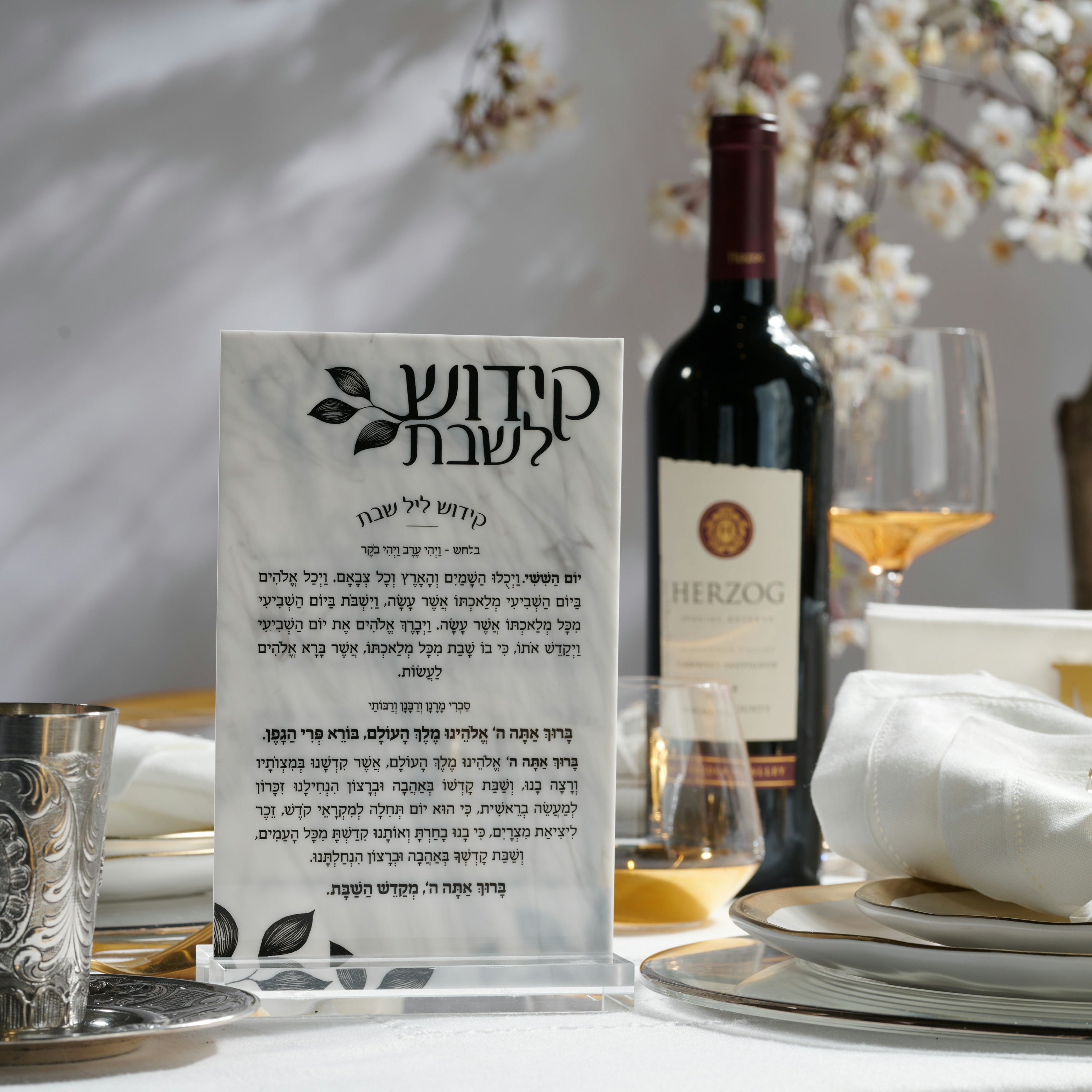 A kiddush L'shabbos displayed on a table setting, with a wine bottle, glass, plates, and flowers in the background - Zstander