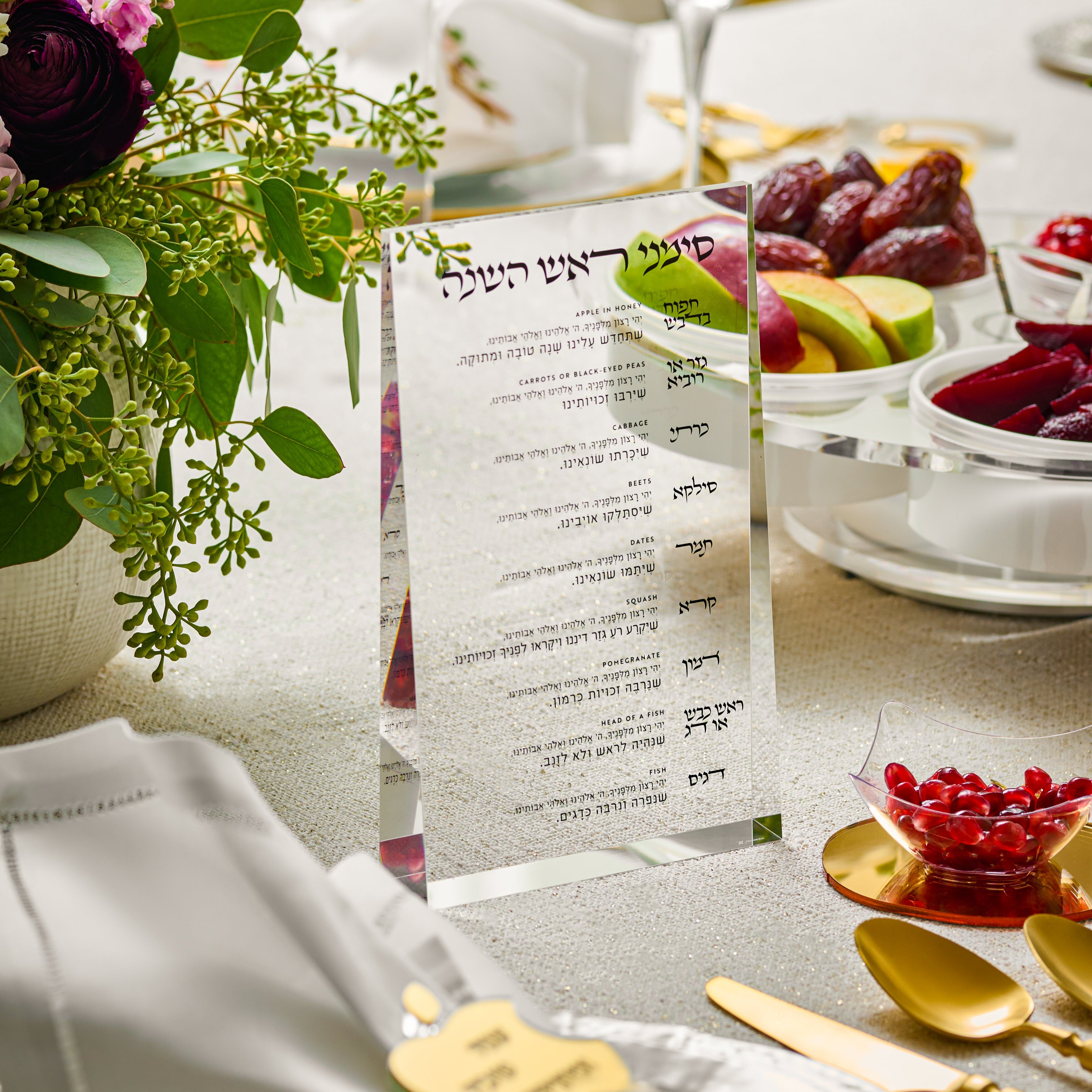 Dining table setting with a transparent black text prism lucite simanim card, flowers, and fruit - Zstander