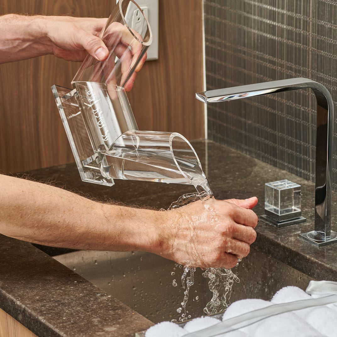 Person washing hands with a dual spout washing cup under a modern kitchen faucet with clear soap dispenser - Zstander