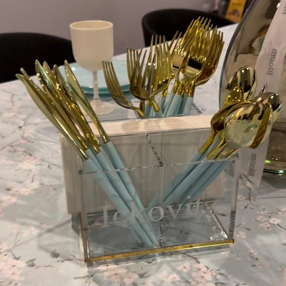Gold cutlery set in a clear glass holder on a floral tablecloth - Zstander