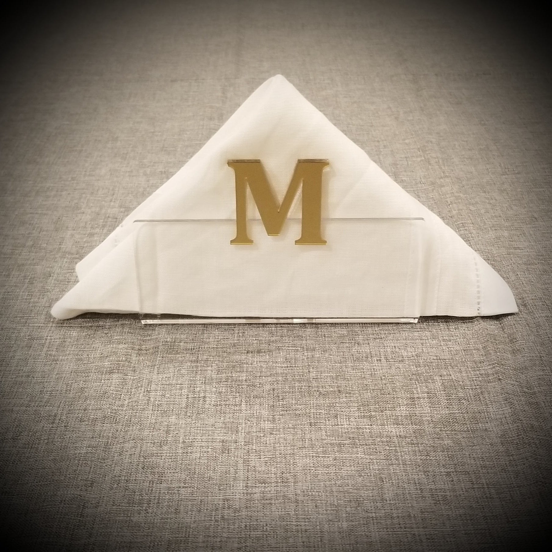 Clear acrylic napkin holder with gold letter 'M' on a burlap background - Zstander