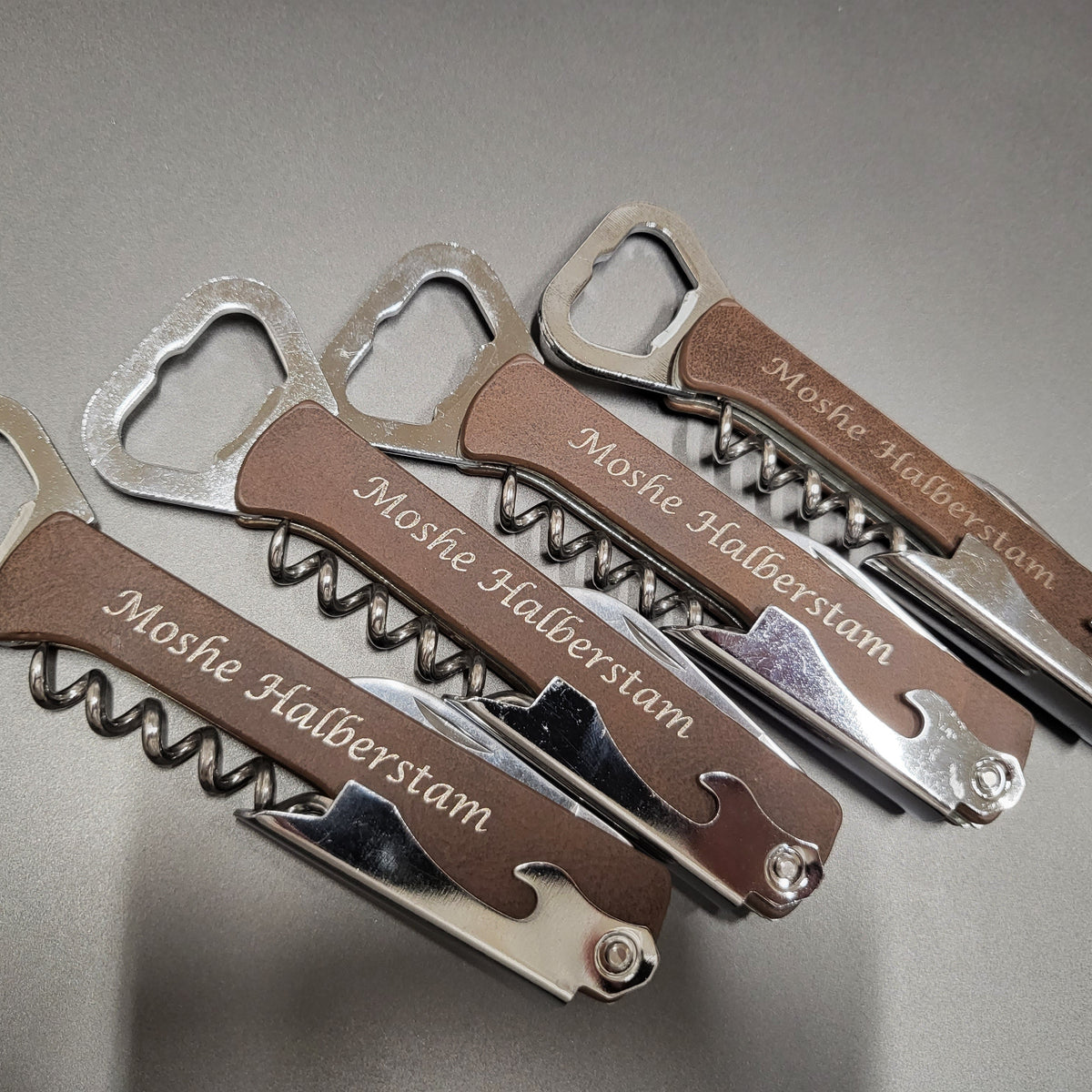4 corkscrews on a table with the name Moshe Halberstam engraved on each one.