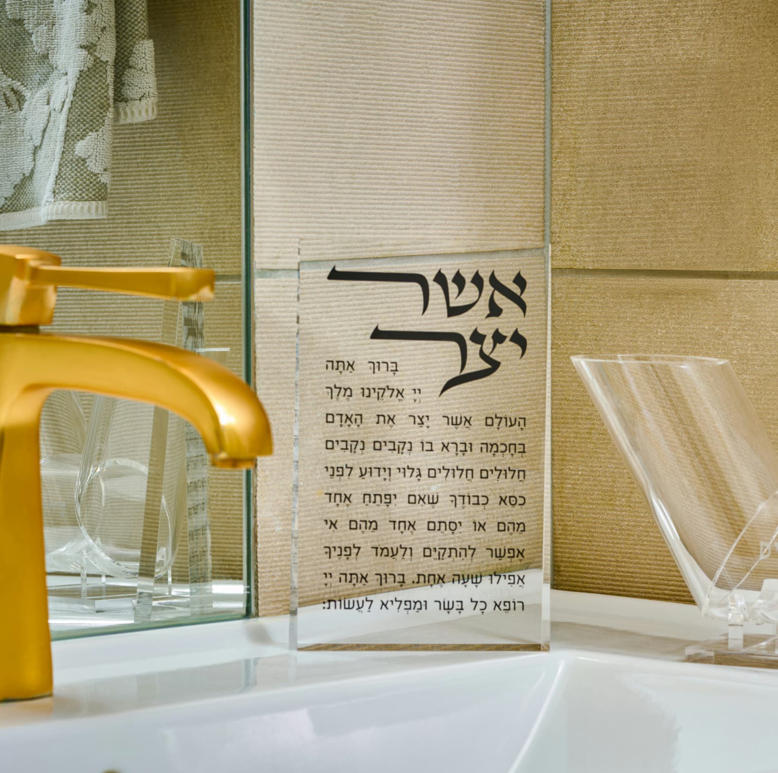 Clear acrylic asher yatzar with Hebrew text on a bathroom wall next to a gold faucet - Zstander