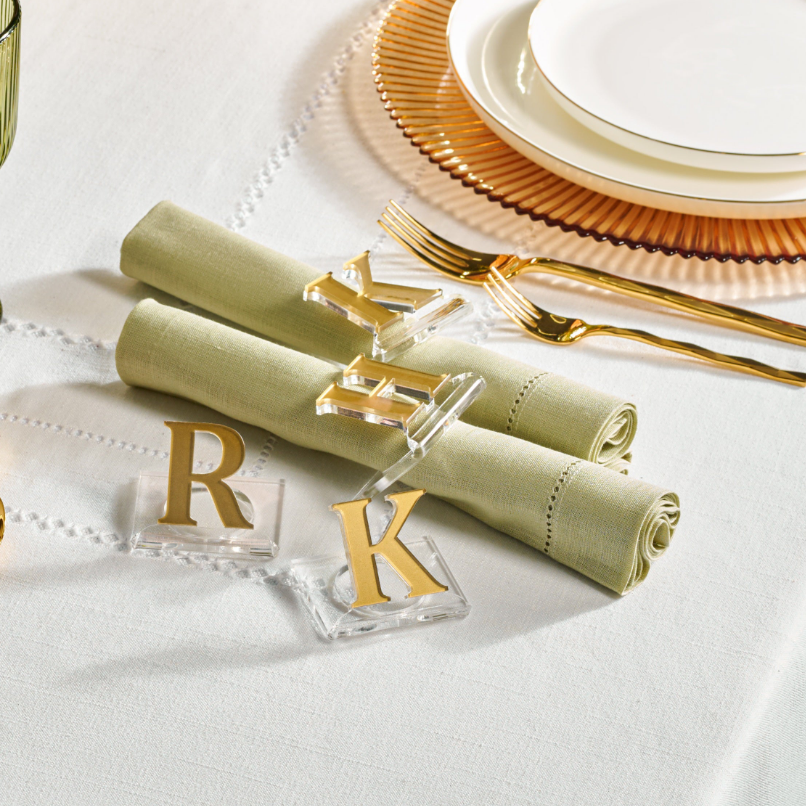 A set of monogrammed lucite napkin rings displayed on a table setting, with the letter 'R' initial. The napkin rings are in gold color, and they are holding a green napkin rolled up - Zstander