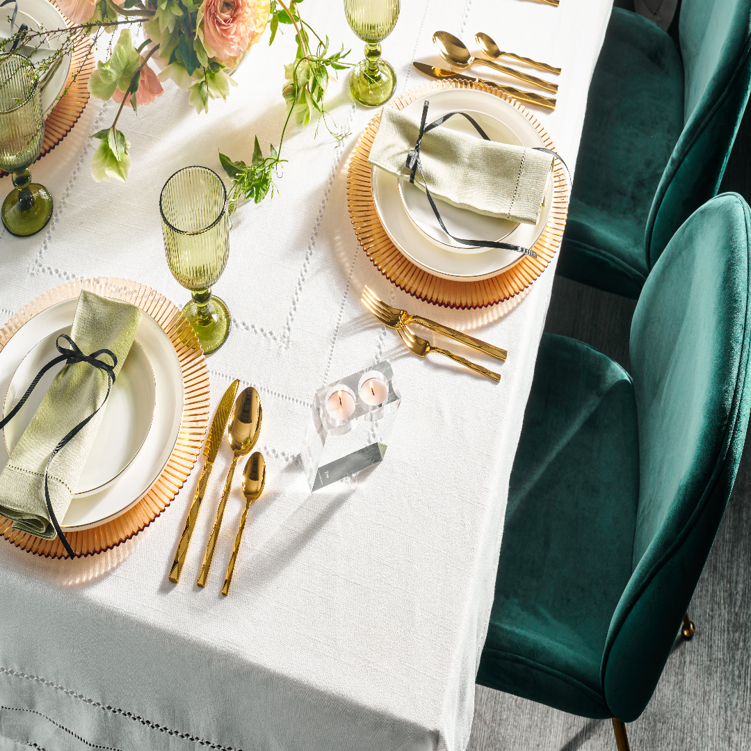 Elegant table setting with gold cutlery, green glasses, and white plates on a white tablecloth - Zstander