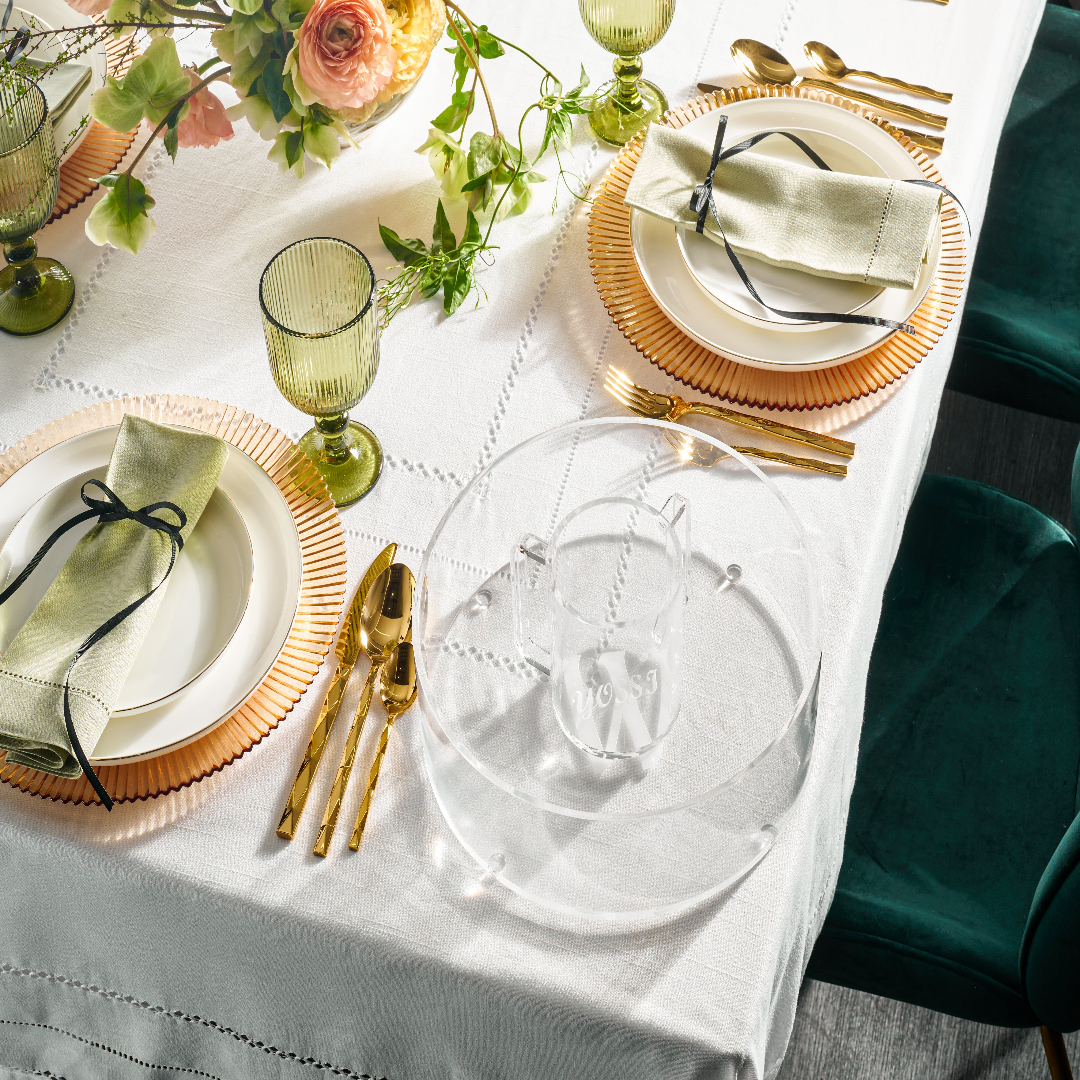 Elegant table setting with gold cutlery, green glasses, and decorative plates on a white tablecloth - Zstander