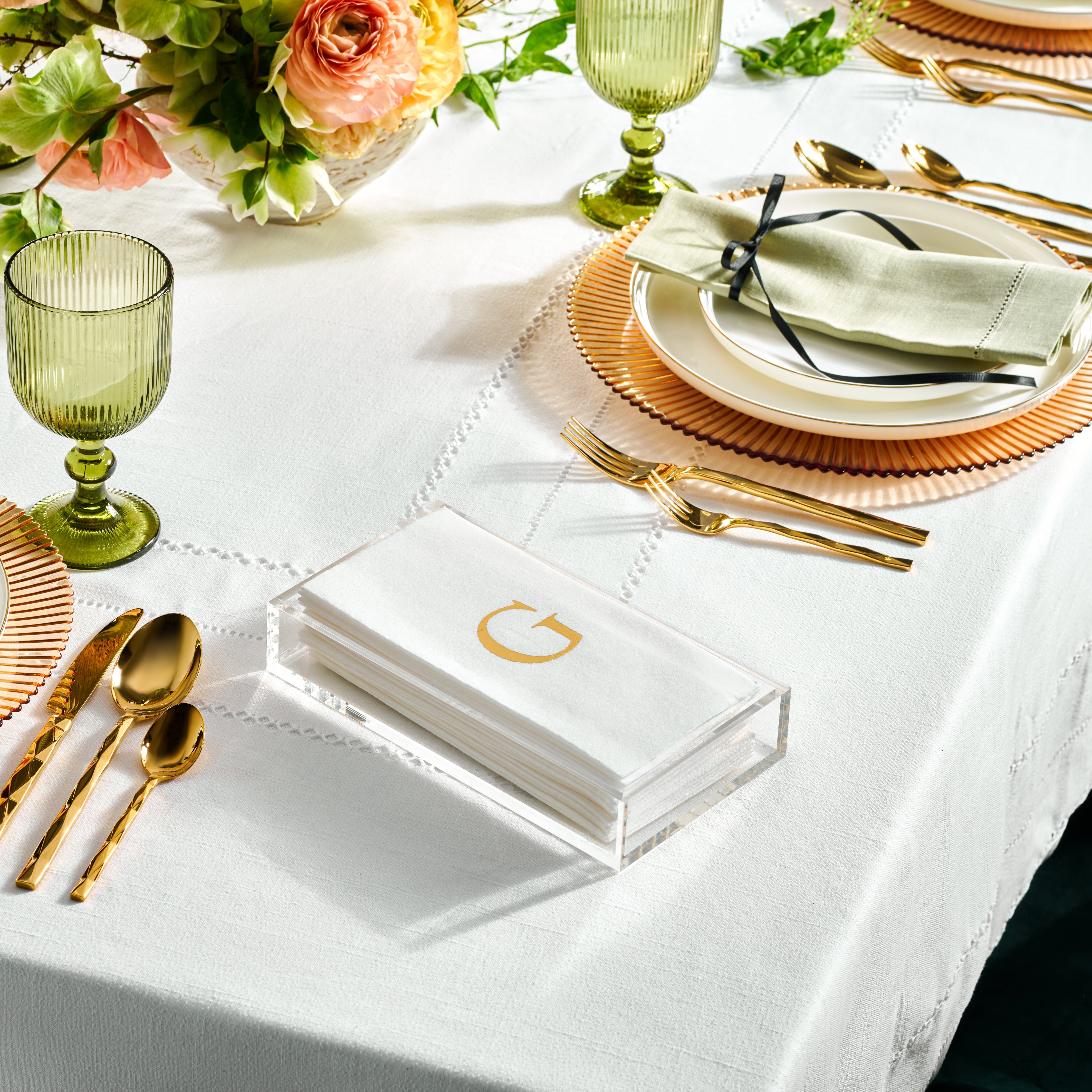 A set of white linen napkins with a gold monogram, displayed on a table with dishes and silverware - Zstander