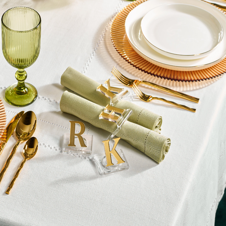 Elegant table setting with green glasses, gold cutlery, and white plates on a white tablecloth - Zstander