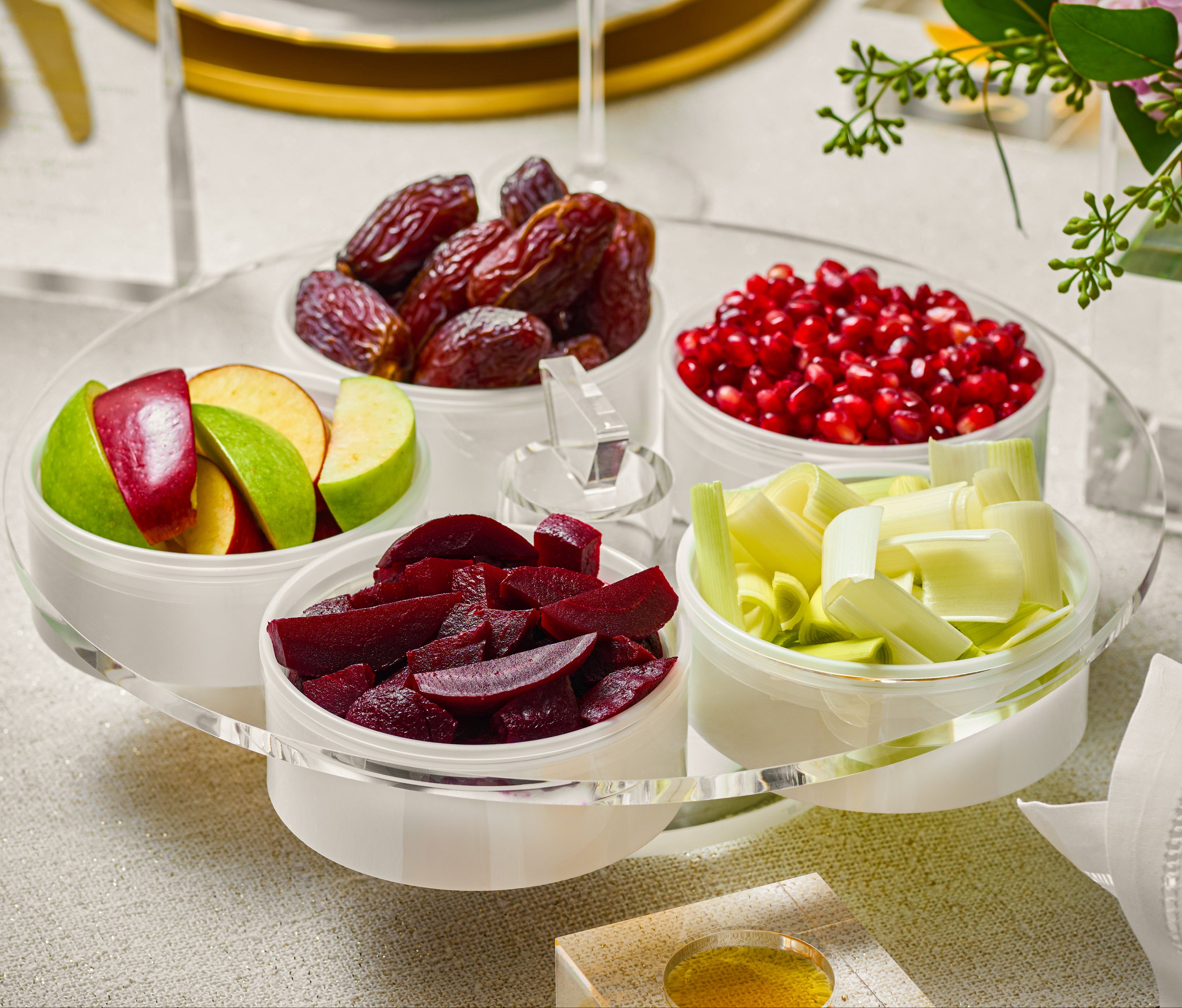 Assorted dried fruits and vegetables on a clear glass tray with a white napkin and floral decorations.
