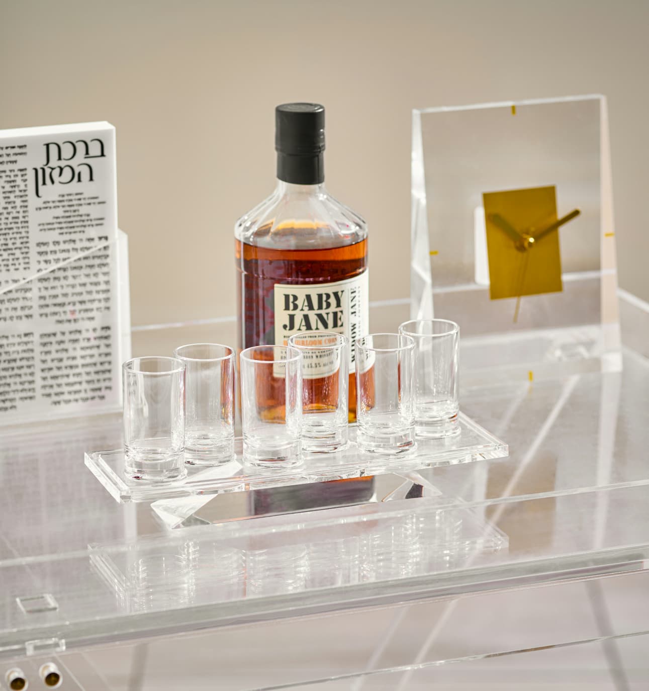 Bottle of 'Baby Jane' whiskey with glasses on a clear acrylic stand against a neutral background - Zstander