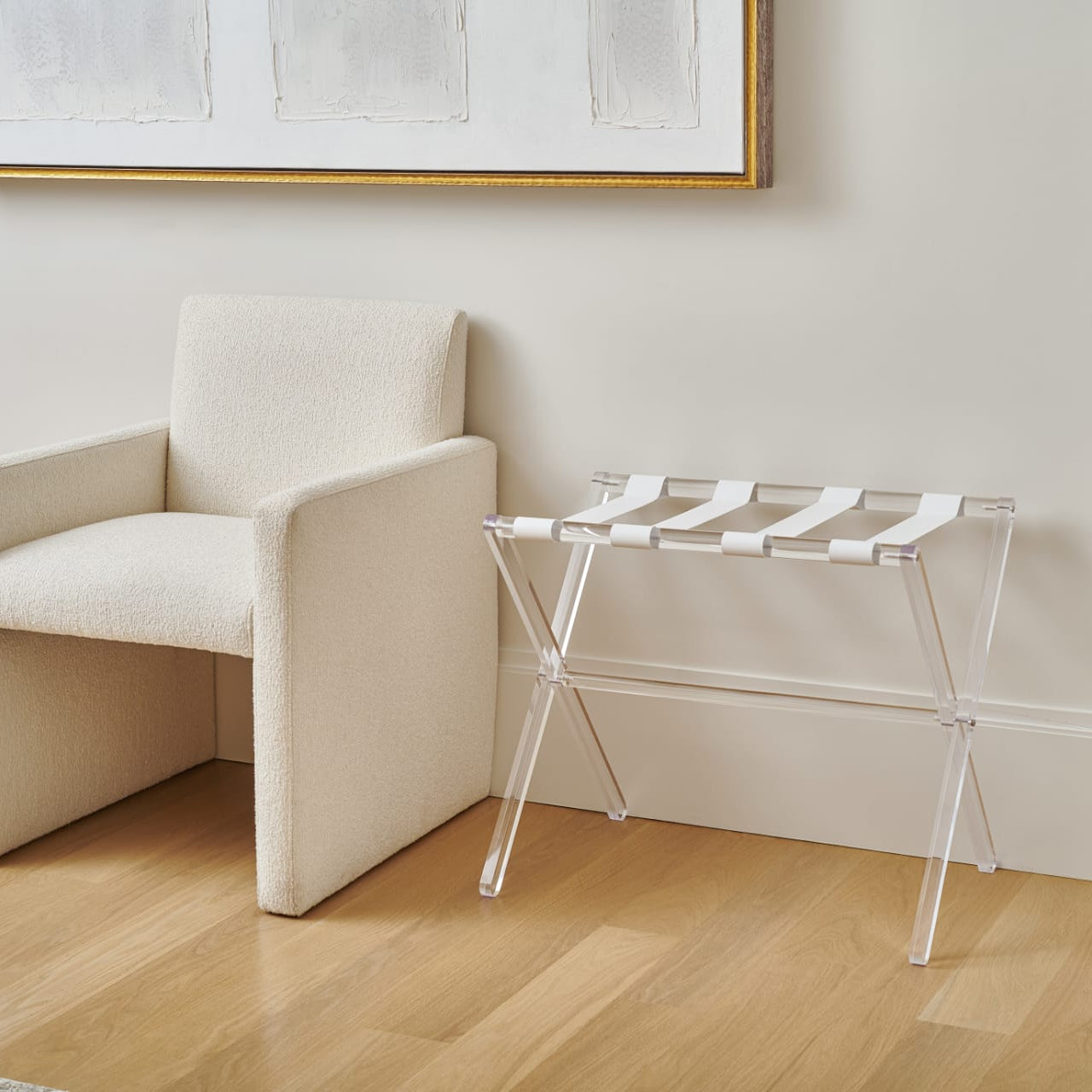 Beige armchair next to a clear  luggage stand with white towels against a white wall -Zstander