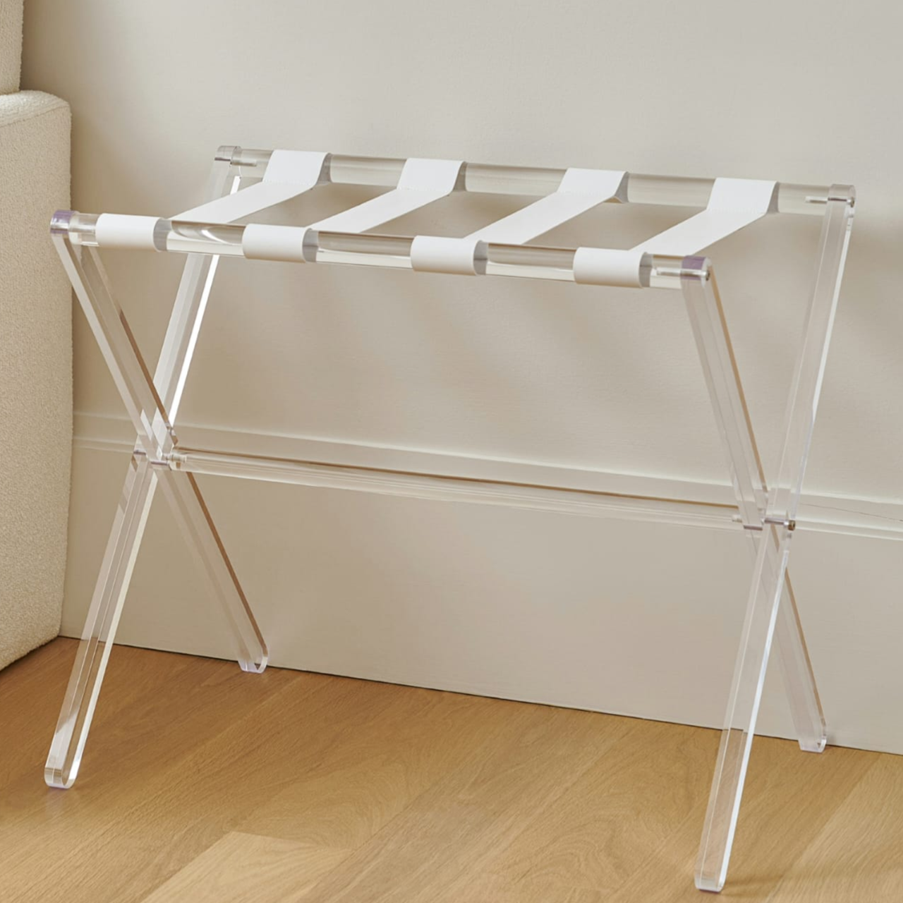 Clear luggage rack with white straps on a wooden floor against a beige wall - Zstander