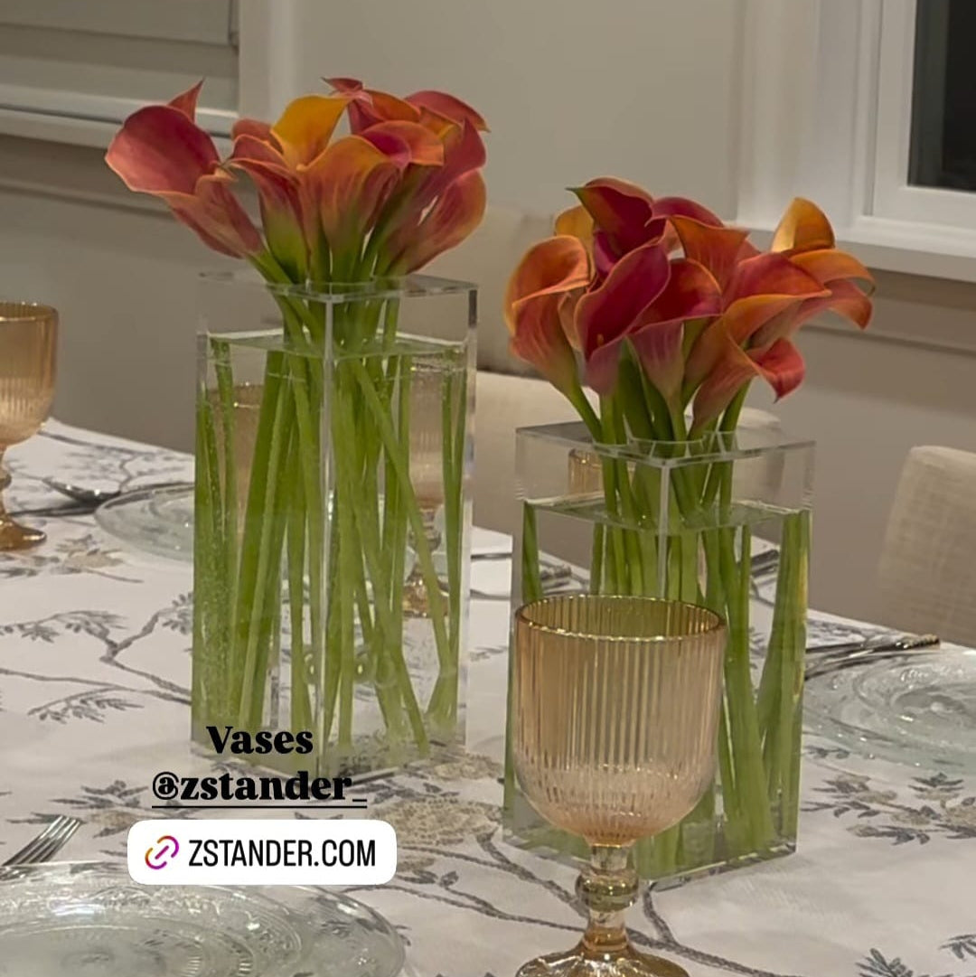 Two glass vases with orange and pink flowers on a dining table with a zstander.com logo.